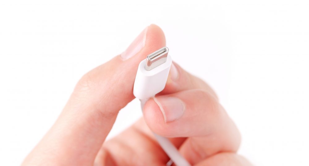 and holding a simple white USB type C mobile phone smartphone charger cable, digital data transfer, charging, power concept, phone accessories. USB C cable plug end detail, macro, extreme closeup