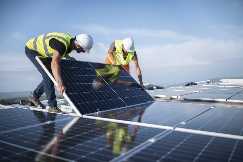 Team of two engineers installing solar panels on roof.